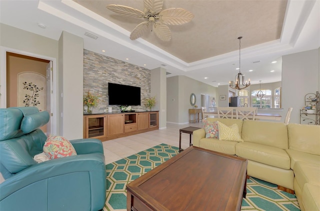 living room with a raised ceiling, light tile patterned flooring, and ceiling fan with notable chandelier