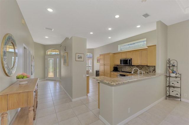 kitchen featuring light tile patterned flooring, light brown cabinetry, kitchen peninsula, light stone countertops, and decorative backsplash