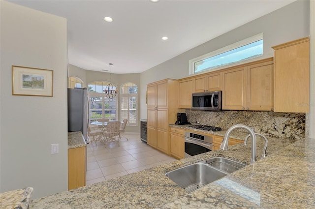 kitchen featuring appliances with stainless steel finishes, light brown cabinetry, decorative light fixtures, tasteful backsplash, and sink