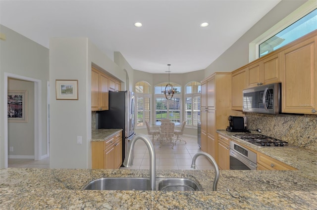 kitchen with sink, hanging light fixtures, stainless steel appliances, light stone countertops, and an inviting chandelier