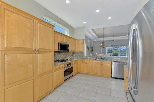 kitchen with a raised ceiling, appliances with stainless steel finishes, light stone counters, and decorative light fixtures