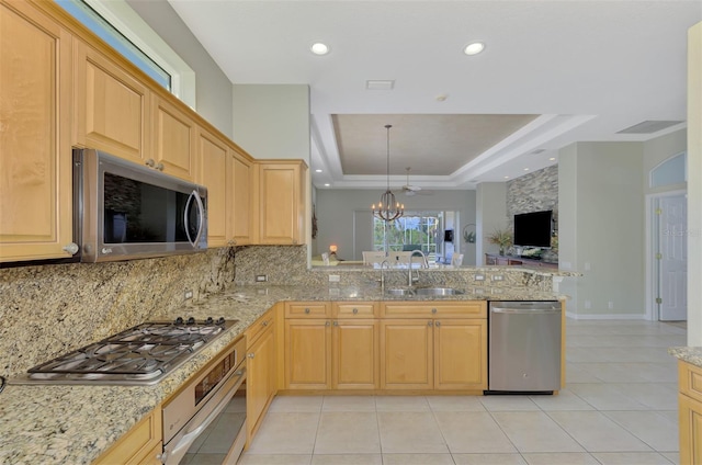 kitchen with a tray ceiling, pendant lighting, sink, kitchen peninsula, and stainless steel appliances