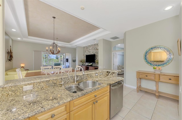 kitchen with stainless steel dishwasher, light brown cabinetry, a raised ceiling, and sink