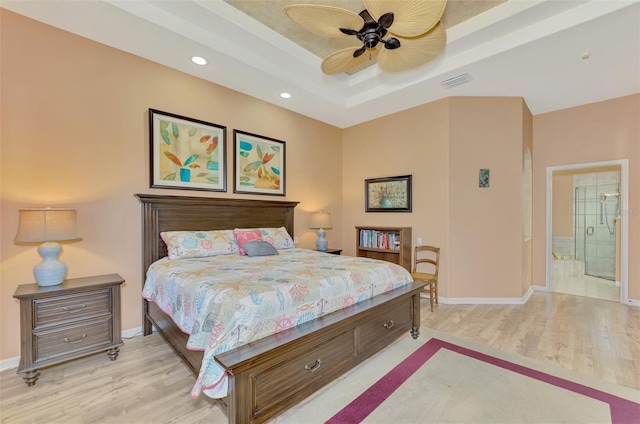 bedroom featuring ceiling fan, connected bathroom, a raised ceiling, and light hardwood / wood-style floors