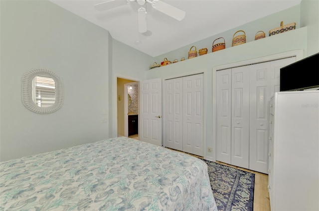 bedroom featuring lofted ceiling, two closets, ceiling fan, and light hardwood / wood-style flooring