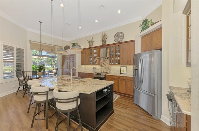 kitchen featuring pendant lighting, wall chimney range hood, sink, a kitchen island with sink, and stainless steel appliances