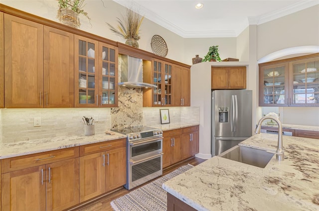 kitchen featuring wall chimney range hood, crown molding, sink, stainless steel appliances, and light stone counters