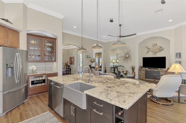 kitchen featuring sink, appliances with stainless steel finishes, pendant lighting, light stone countertops, and a kitchen island with sink