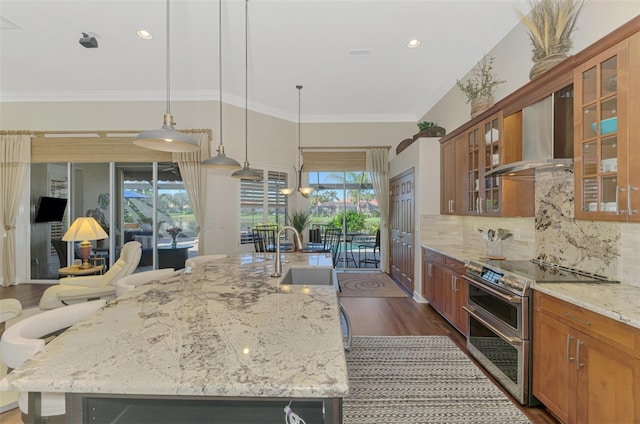 kitchen with pendant lighting, sink, range with two ovens, light stone countertops, and wall chimney range hood