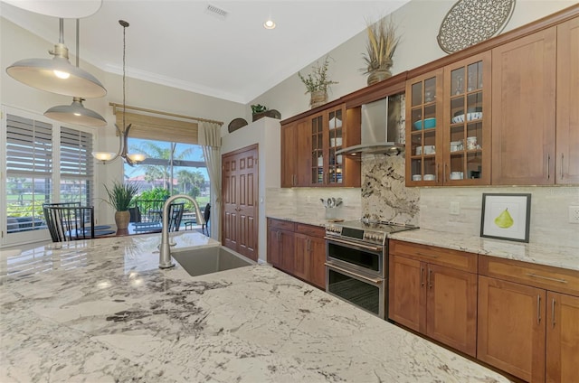 kitchen with wall chimney range hood, sink, hanging light fixtures, light stone countertops, and range with two ovens