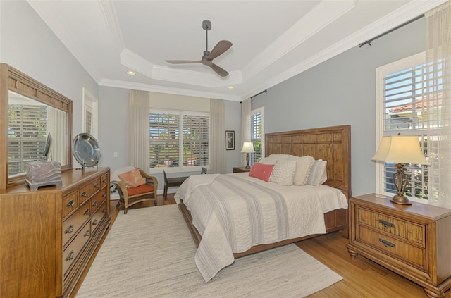 bedroom featuring crown molding, a raised ceiling, ceiling fan, and light wood-type flooring