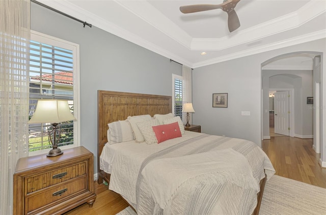 bedroom with a raised ceiling, crown molding, ceiling fan, and light wood-type flooring