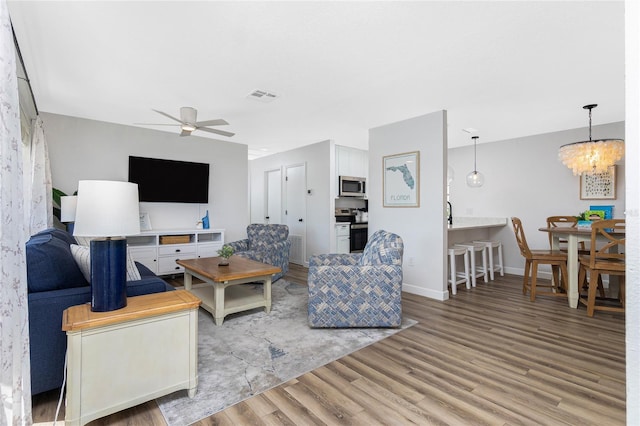 living room featuring ceiling fan with notable chandelier and light hardwood / wood-style floors