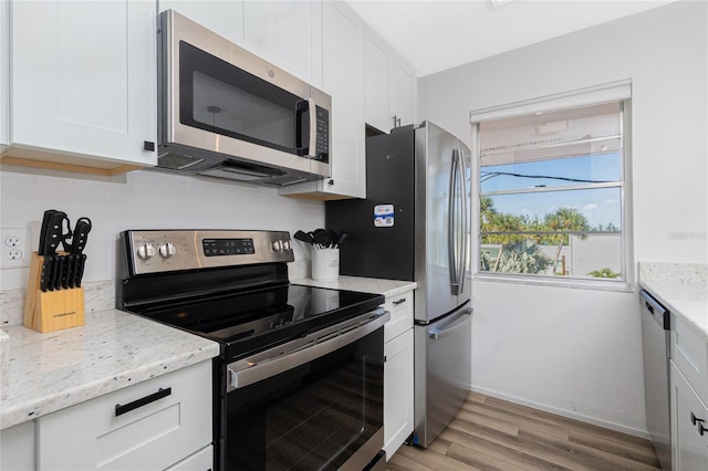 kitchen featuring light stone countertops, white cabinetry, appliances with stainless steel finishes, and light hardwood / wood-style flooring