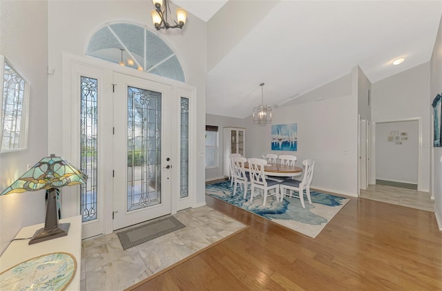 foyer entrance with an inviting chandelier, high vaulted ceiling, and light hardwood / wood-style floors