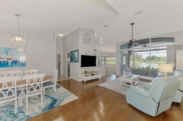 living room with high vaulted ceiling, wood-type flooring, and ceiling fan with notable chandelier