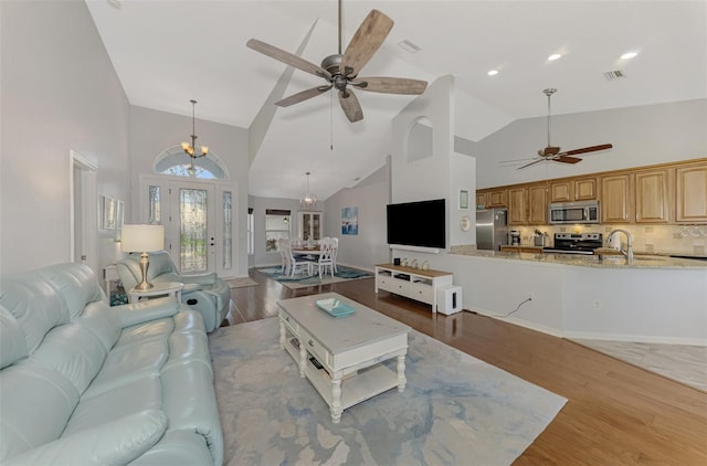 living room featuring sink, ceiling fan with notable chandelier, high vaulted ceiling, and light wood-type flooring