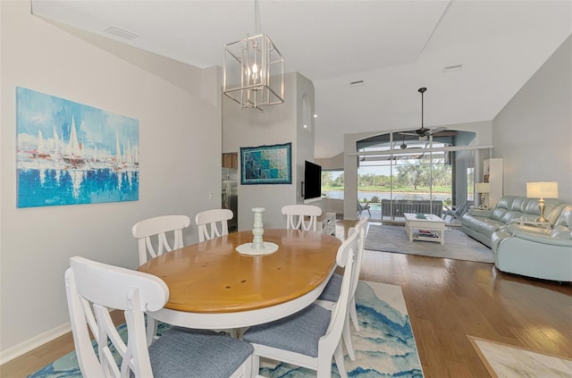 dining area featuring hardwood / wood-style floors, ceiling fan with notable chandelier, and high vaulted ceiling