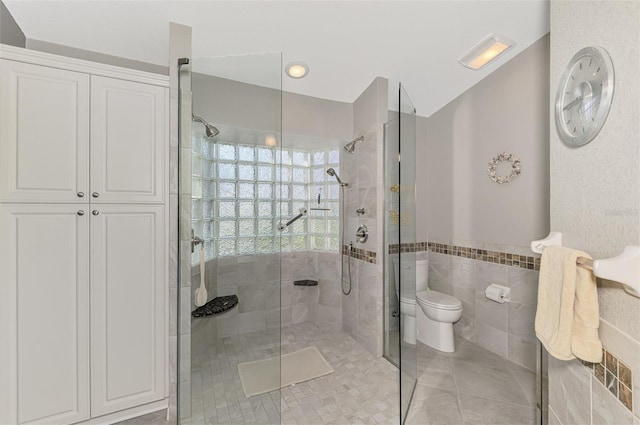 bathroom with tile walls, tile patterned flooring, a shower with shower door, and toilet