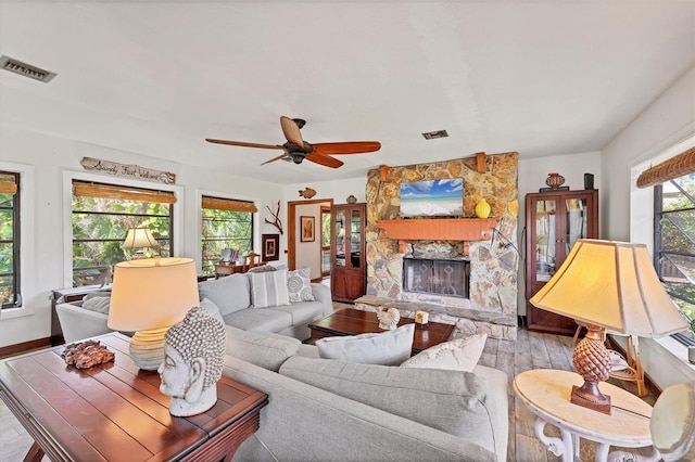 living room featuring ceiling fan, a stone fireplace, and light wood-type flooring