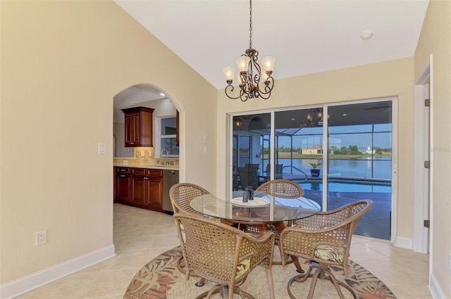 tiled dining space featuring sink, a notable chandelier, vaulted ceiling, and a water view