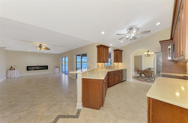 kitchen featuring lofted ceiling, ceiling fan with notable chandelier, stainless steel appliances, decorative backsplash, and kitchen peninsula