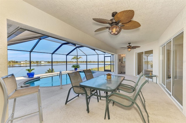 outdoor pool with glass enclosure, a patio area, a water view, and ceiling fan