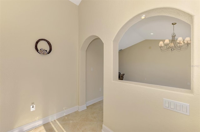 hallway with baseboards, arched walkways, lofted ceiling, an inviting chandelier, and tile patterned flooring