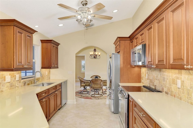 kitchen featuring arched walkways, stainless steel appliances, a sink, light countertops, and brown cabinetry