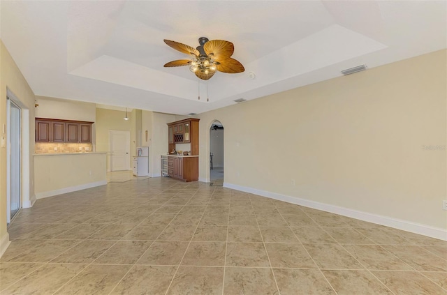 unfurnished living room with visible vents, a tray ceiling, a ceiling fan, and baseboards