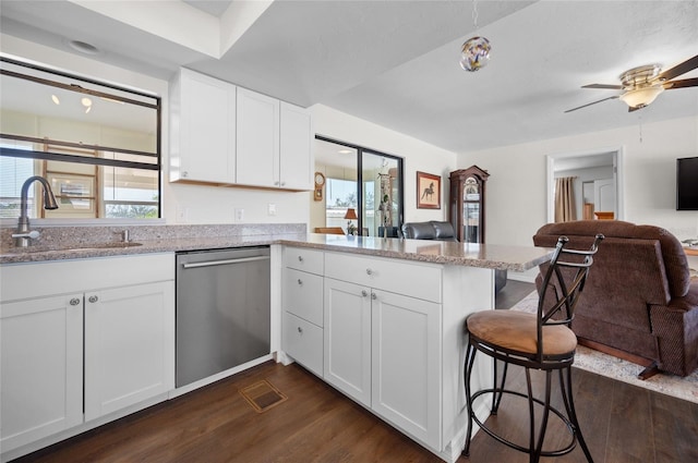 kitchen with a breakfast bar area, white cabinetry, dishwasher, kitchen peninsula, and light stone countertops