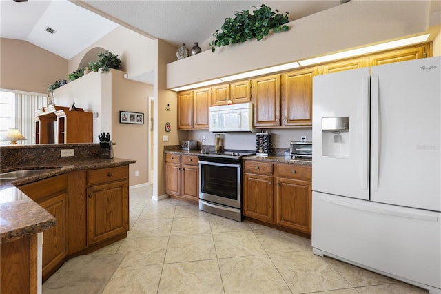 kitchen featuring light tile patterned flooring, white appliances, dark stone counters, and vaulted ceiling