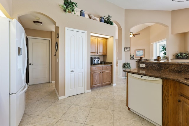 kitchen with dark stone countertops, white appliances, ceiling fan, and light tile patterned flooring