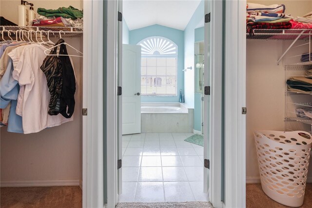 bathroom featuring a relaxing tiled tub, tile patterned flooring, and vaulted ceiling