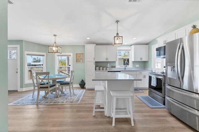 kitchen with a kitchen island, pendant lighting, stainless steel appliances, light hardwood / wood-style floors, and white cabinets