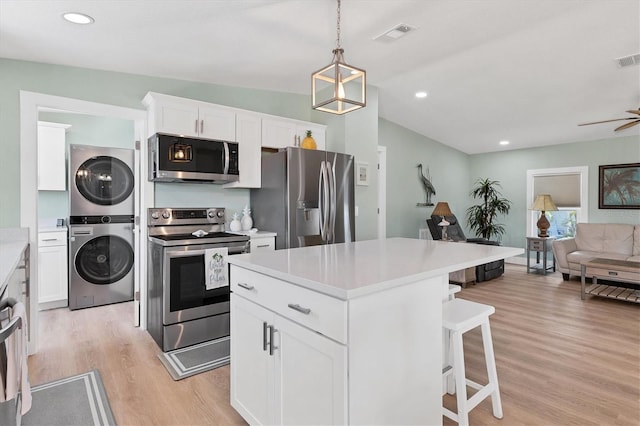 kitchen featuring hanging light fixtures, stainless steel appliances, stacked washer and clothes dryer, and white cabinets