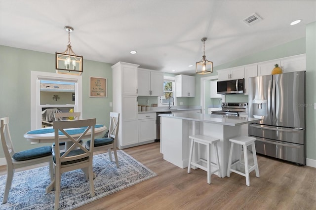 kitchen featuring stainless steel appliances, a center island, white cabinets, and decorative light fixtures