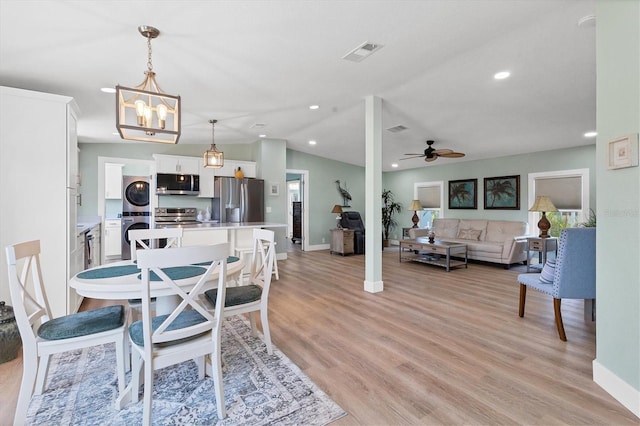 dining space featuring stacked washer and dryer, vaulted ceiling, light hardwood / wood-style flooring, a wealth of natural light, and ceiling fan with notable chandelier