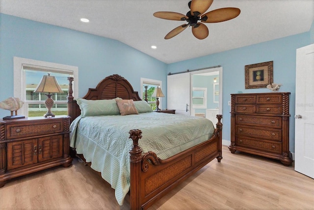 bedroom with vaulted ceiling, a barn door, ceiling fan, and light wood-type flooring