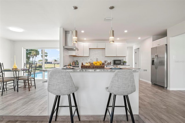 kitchen with white cabinetry, backsplash, stainless steel refrigerator with ice dispenser, decorative light fixtures, and wall chimney exhaust hood