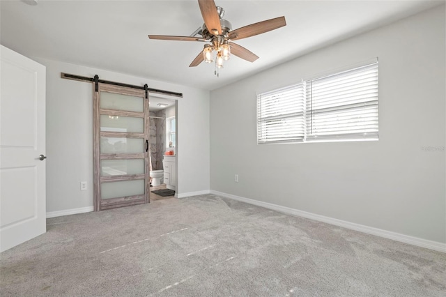 unfurnished bedroom with ceiling fan, light colored carpet, connected bathroom, and a barn door