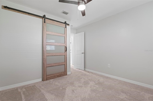 unfurnished room with a barn door, light colored carpet, and ceiling fan