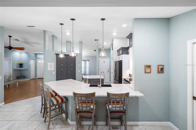 kitchen with pendant lighting, stainless steel fridge, a kitchen breakfast bar, light stone counters, and kitchen peninsula