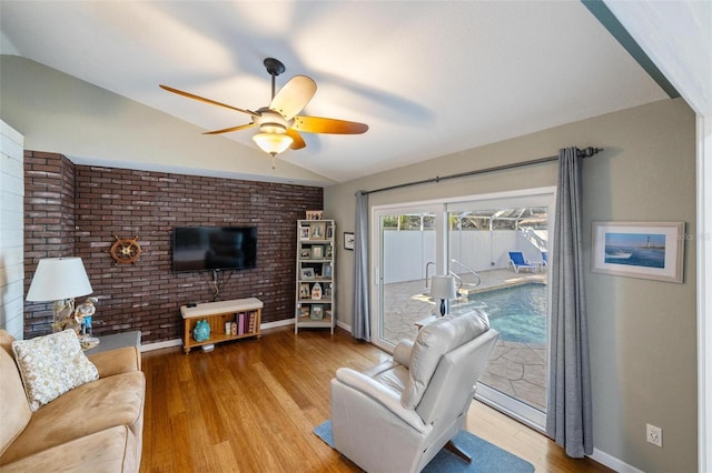 living room with hardwood / wood-style flooring, vaulted ceiling, ceiling fan, and brick wall