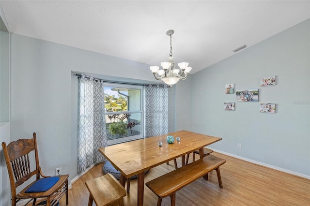 dining area featuring a notable chandelier, vaulted ceiling, and light wood-type flooring