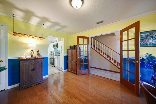 interior space with stainless steel appliances, wood-type flooring, crown molding, and french doors