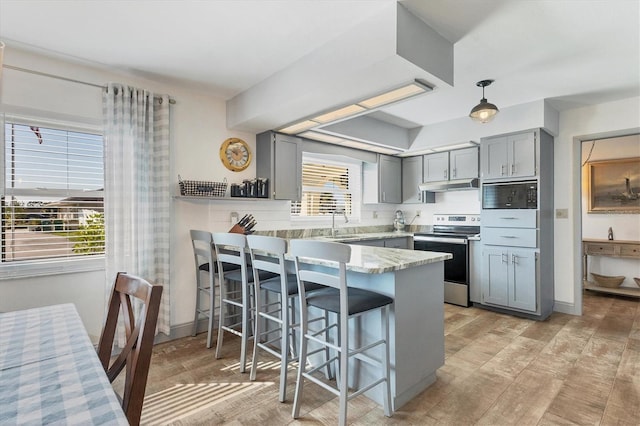 kitchen with stainless steel electric range oven, a breakfast bar, gray cabinetry, hanging light fixtures, and kitchen peninsula