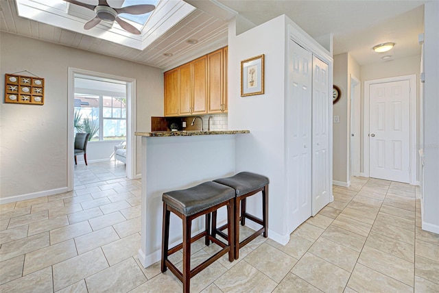 kitchen with ceiling fan, a skylight, tasteful backsplash, light stone counters, and a kitchen bar