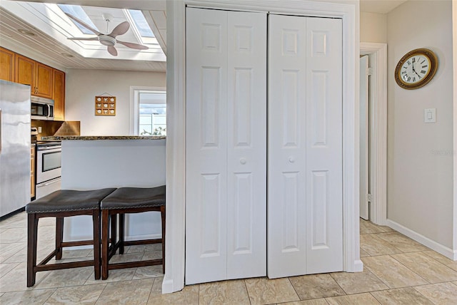 kitchen with dark stone countertops, a skylight, stainless steel appliances, and ceiling fan