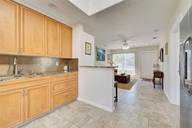 kitchen featuring sink, tasteful backsplash, light stone counters, stainless steel fridge, and ceiling fan